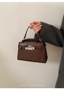 Brown crocodile-patterned small handbag held against a minimalist wall
