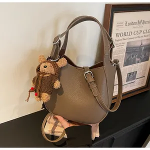 Elegant taupe pebbled leather bucket bag featuring a cute teddy bear charm accessory