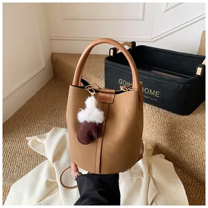 Detailansicht einer braunen Wildleder-Eimertasche im Retro-Stil mit Plüsch-Anhänger