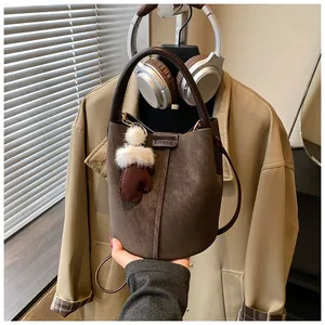Detail einer braunen Vintage-Eimertasche mit flauschigem Handschuh-Anhänger für Damen.