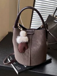 Braune Vintage-Eimertasche mit Plüschhandschuh-Anhänger auf Buch
