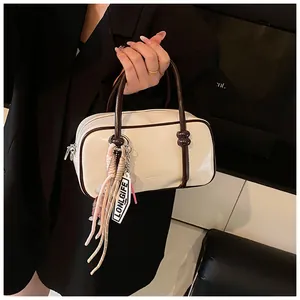 Detailed view of elegant cream pillow bag with brown trim and stylish tassel charm