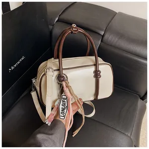 Close-up of a stylish cream mini pillow handbag with brown trim and long charms