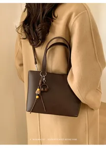 Macro view of a vintage dark brown handbag with minimalist charms worn on a beige coat.