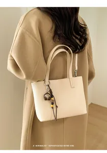 Elegant beige minimalist handbag shown as a shoulder bag on a model in a wool coat