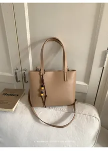 Dettaglio borsa tote beige minimalista con ciondolo di perline e tracolla lunga.