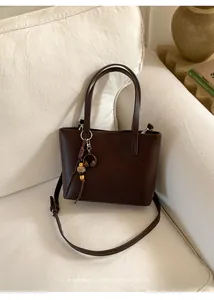 Vintage brown leather tote bag with minimalist charm shown on a cream sofa backdrop.