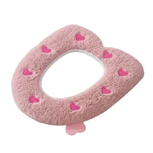 Soft pink plush toilet seat cover featuring cute embroidered heart patterns and pull tab