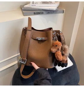 Close-up view of a brown pebble-textured bucket bag featuring a cute alpaca keychain.