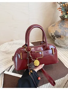 Dettaglio di una borsa a conchiglia bordeaux vintage con fibbia e ciondoli.