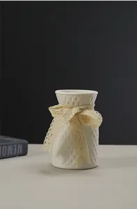 Close-up detail of a white ceramic lattice textured vase with decorative lace ribbon