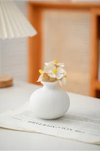 Close-up of minimalist white ceramic vase with artificial daisy flowers on newspaper
