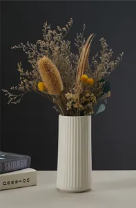Detail shot of a white fluted ceramic vase with dried flowers in a home setting.
