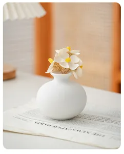 Detailed close-up view of a minimalist white ceramic vase with delicate faux flowers