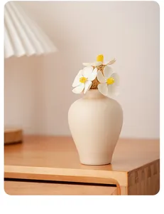 Close-up of minimalist beige ceramic vase with white flowers on wooden table