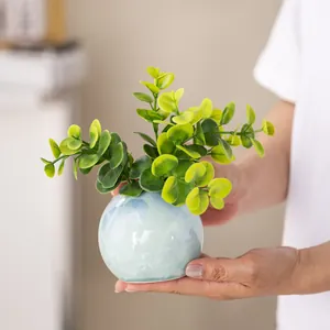 Hands holding a crystalline glaze ceramic flower vase with artificial green plant.