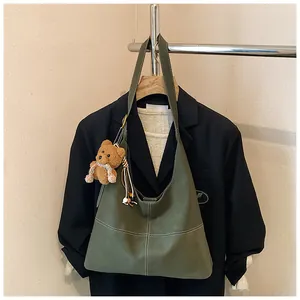 Detalle del bolso tote vintage verde oliva con colgante de oso en una percha de traje