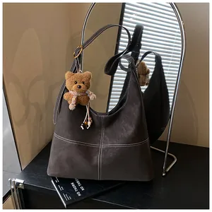 Primer plano de bolso hobo marrón retro con colgante de oso y costuras en contraste