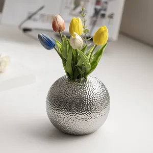 Gedetailleerd beeld van een zilveren gehamerde bolvormige vaas met kunsttulpen.