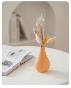 Minimalist peach ceramic vase featuring dried grass decor on a white textured table