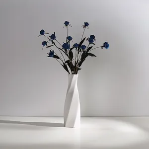 Minimalist white ceramic vase with twisted design and artificial blue roses for home decor.