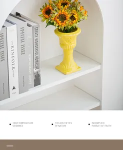 Bright yellow ceramic Roman column decorative flower vase on a white bookshelf.