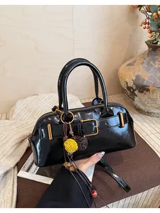 Dettaglio della borsa retrò nera lucida con fibbia dorata e ciondolo a pompon.
