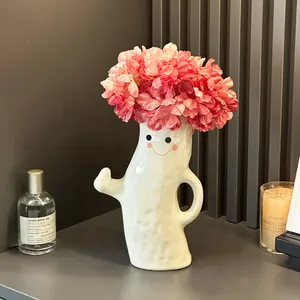 Handmade white ceramic ghost vase with cute face and arms holding pink flowers