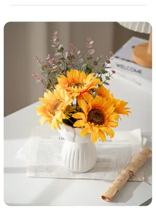 Close-up of vibrant artificial sunflowers in a white fluted ceramic vase on a table
