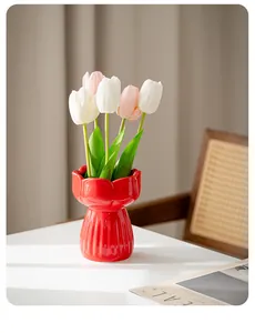 Detailed view of a bright red tulip-shaped ceramic vase with artificial flowers on a desk