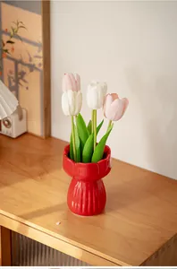 Red tulip-shaped ceramic vase on a wooden desk with realistic artificial flowers