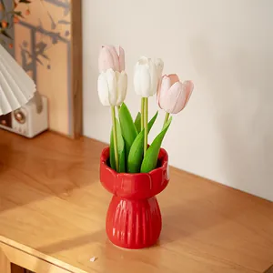 Elegant red ceramic tulip flower vase with artificial pink and white tulips on a wooden desk