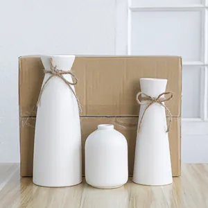 Minimalistische witte keramische vazenset van drie met decoratieve strikken van henneptouw