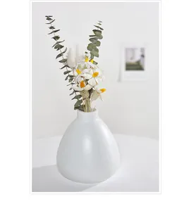 Vase en céramique blanc minimaliste avec fleurs séchées dans un décor de maison confortable