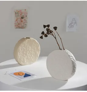 Set of two minimalist Nordic white ceramic vases with dimpled texture on a white pedestal