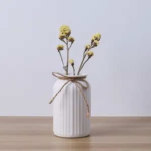 Modern minimalist white ceramic vase with yellow dried flowers on wooden table surface.
