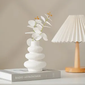 Modern minimalist white tiered ceramic vase with artificial leaves on a decorative book