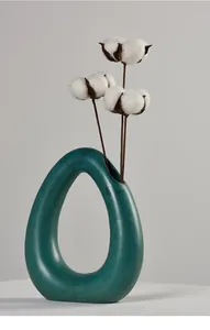 Macro view of a teal teardrop ceramic vase decorated with dried cotton flowers.