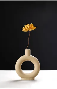 Detailopname van een matte beige donut-keramische vaas met een mooie gele droogbloem.