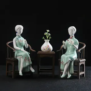 Par de figuras de damas chinas de cerámica clásica en qipao verde en sillas en miniatura.