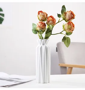 Detailed view of a minimalist white geometric ceramic vase decorated with artificial orange roses