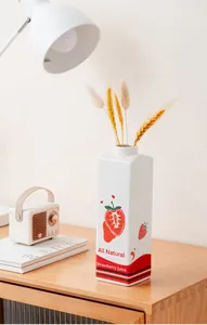 Detailopname van een keramische aardbeienmelkpakvaas op een houten bureau thuis