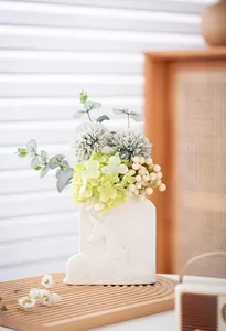 Detailed view of white ceramic vase with embossed deer pattern and artificial floral arrangement