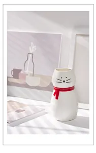 Minimalistische witte keramische kattenvaas met rode sjaal in een gezellig huis.
