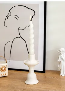 White ceramic candlestick holder with a lit spiral candle in a cozy home setup