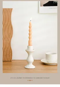 Close-up of a white ceramic candle holder with a lit peach spiral candle on a wooden table