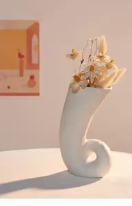 Vue détaillée d'un vase en céramique blanc incurvé avec des fleurs séchées au ton chaud