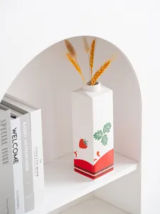 Keramische aardbeienvaas in de vorm van een melkpak met droogbloemen op witte plank