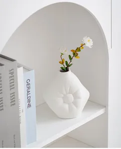 Vase en céramique blanc en forme de soleil posé sur une étagère blanche arquée