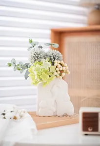 Nahaufnahme einer weißen Keramik-Elefanten-Vase mit grünem künstlichem Blumenstrauß